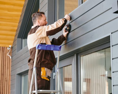 Young man in uniform holding alarm system while standing on ladder