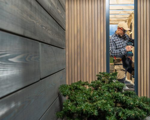 Modern Custom Garden Shed Building Performed by Caucasian Construction Worker in His 40s. Window Installing. Small Architecture Theme.